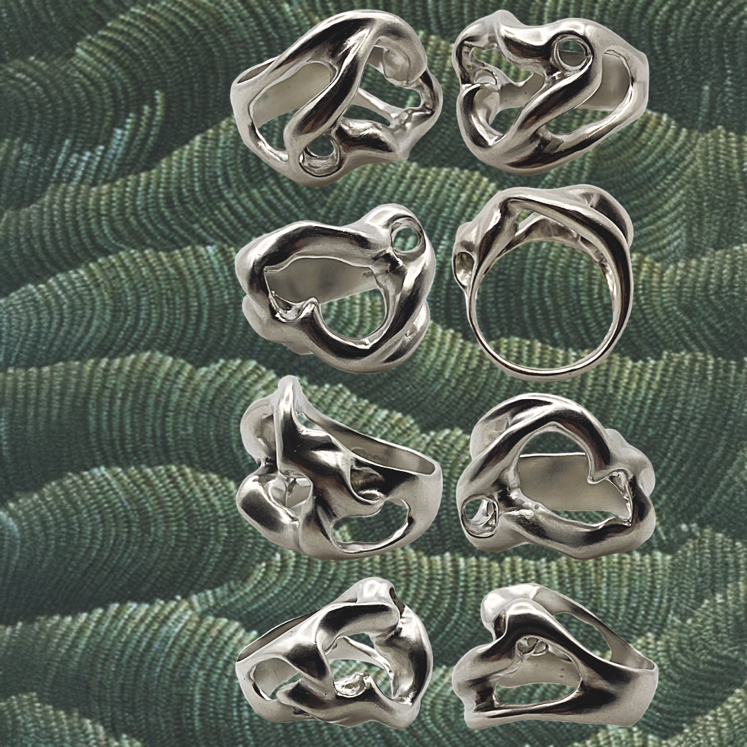 Silver rings with organic designs on a green textured fabric background