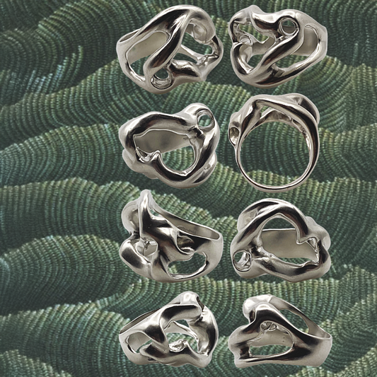 Silver rings with organic designs on a green textured fabric background