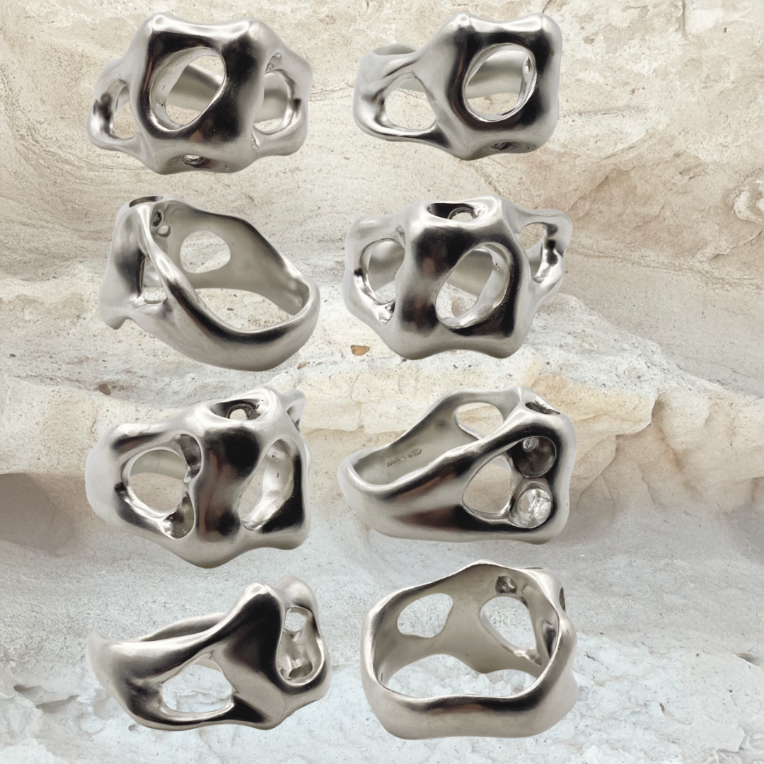 Collection of silver rings with unique designs on a textured surface